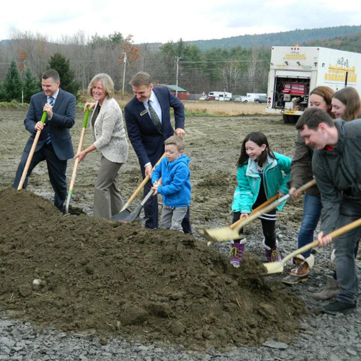 Adults and children shoveling dirt at groundbreaking site
